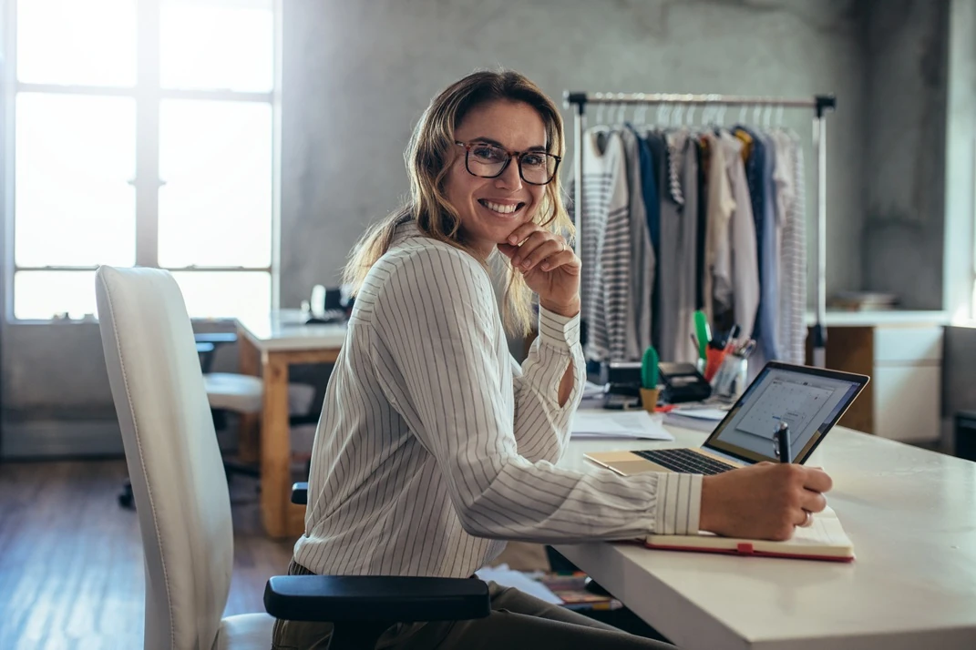 Gen AI for small businesses and the use cases to improve productivity 8 A smiling business woman at her workstation, writing in a notebook and using a laptop, reflecting the creativity and productivity inspired by Lyfe AI.