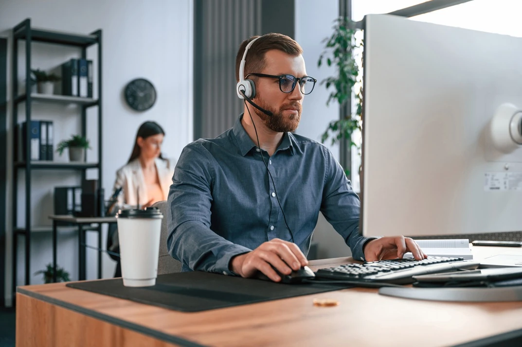 IT support using a headset while working on a computer in an office. Powered by LYFE AI