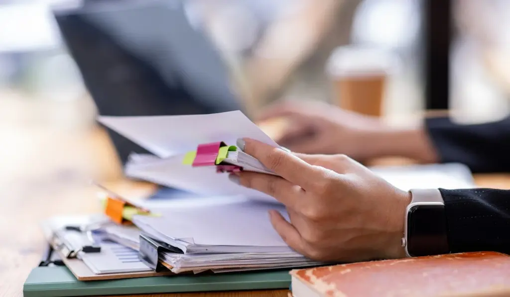 A professional handling paperwork while managing digital documents, illustrating the administrative overhead faced by allied health professionals and how Lyfe AI can help.