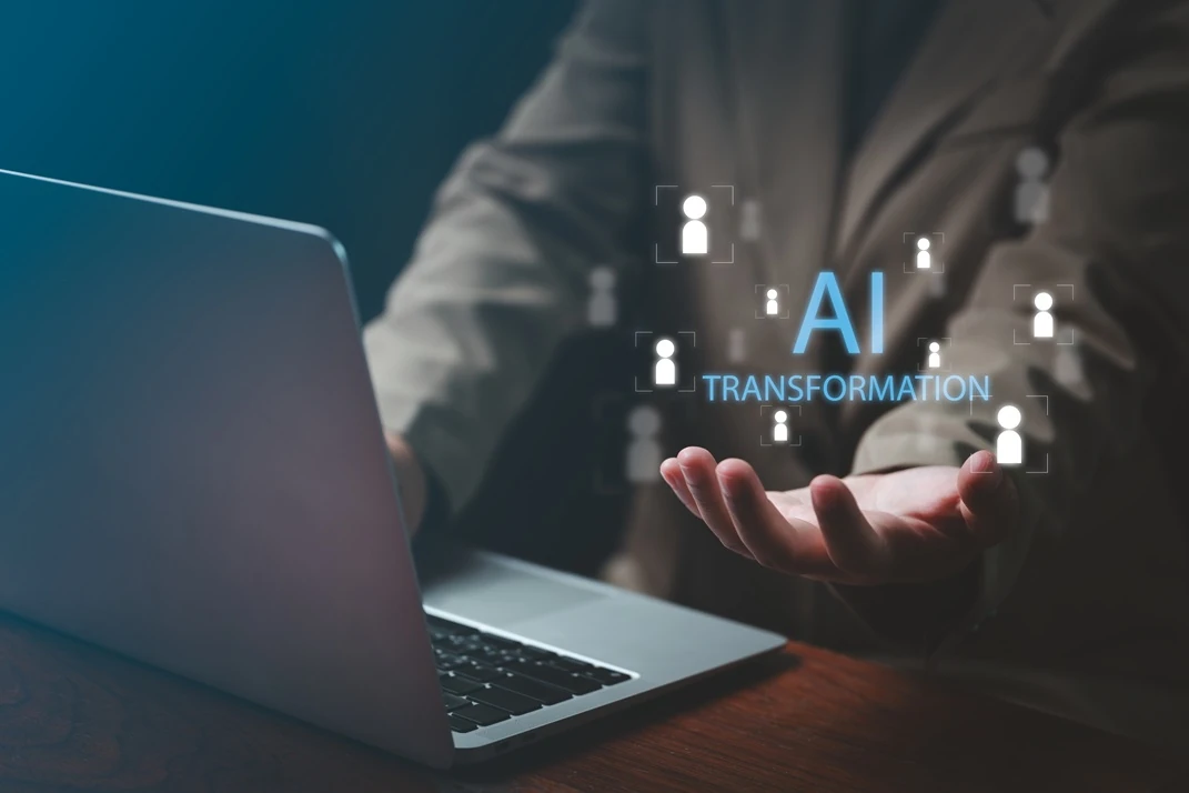 A businessman’s hand reaching out with the words "AI Transformation" and user icons floating above a laptop, illustrating the impact of Lyfe AI on modern business.