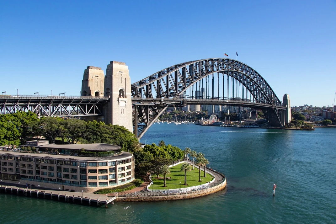 View of the Sydney Harbour Bridge from the water with surrounding greenery.